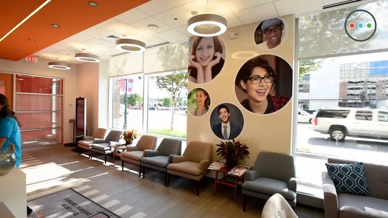 Bright and welcoming orthodontic office interior featuring smiling patients' faces on the wall, comfortable seating area, and large windows for natural light.