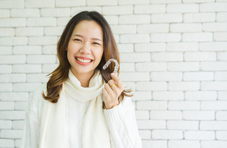 Woman smiling and holding her Invisalign aligners at Behl Orthodontics