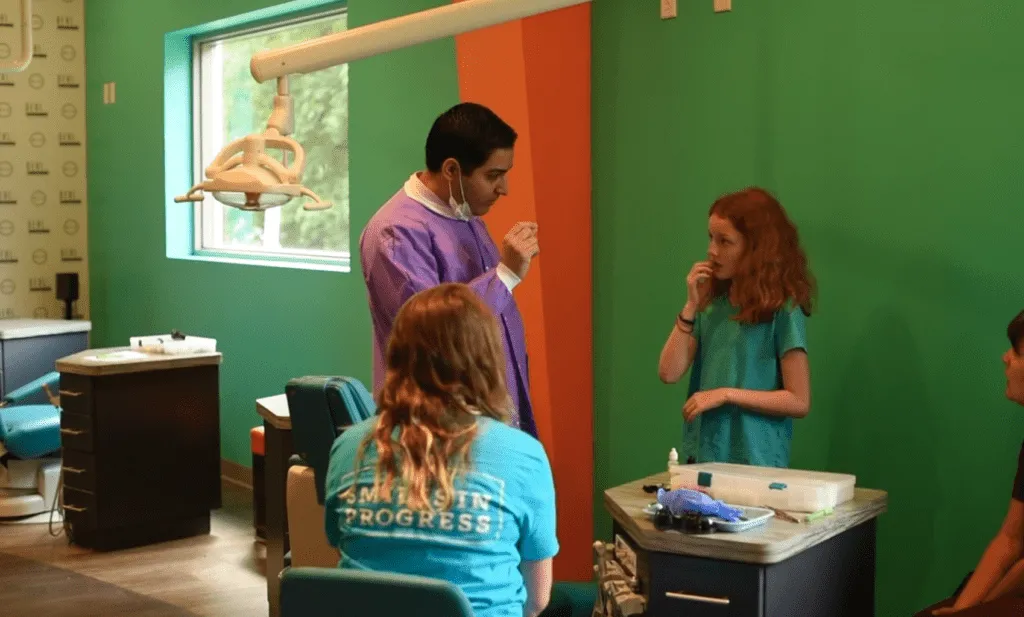 Child receiving dental care from orthodontist in colorful pediatric dental office, with staff assisting and discussing treatment options.