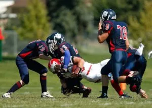 Football players tackling an opponent on a grassy field, showcasing sports injuries and the importance of protective gear like mouth guards.